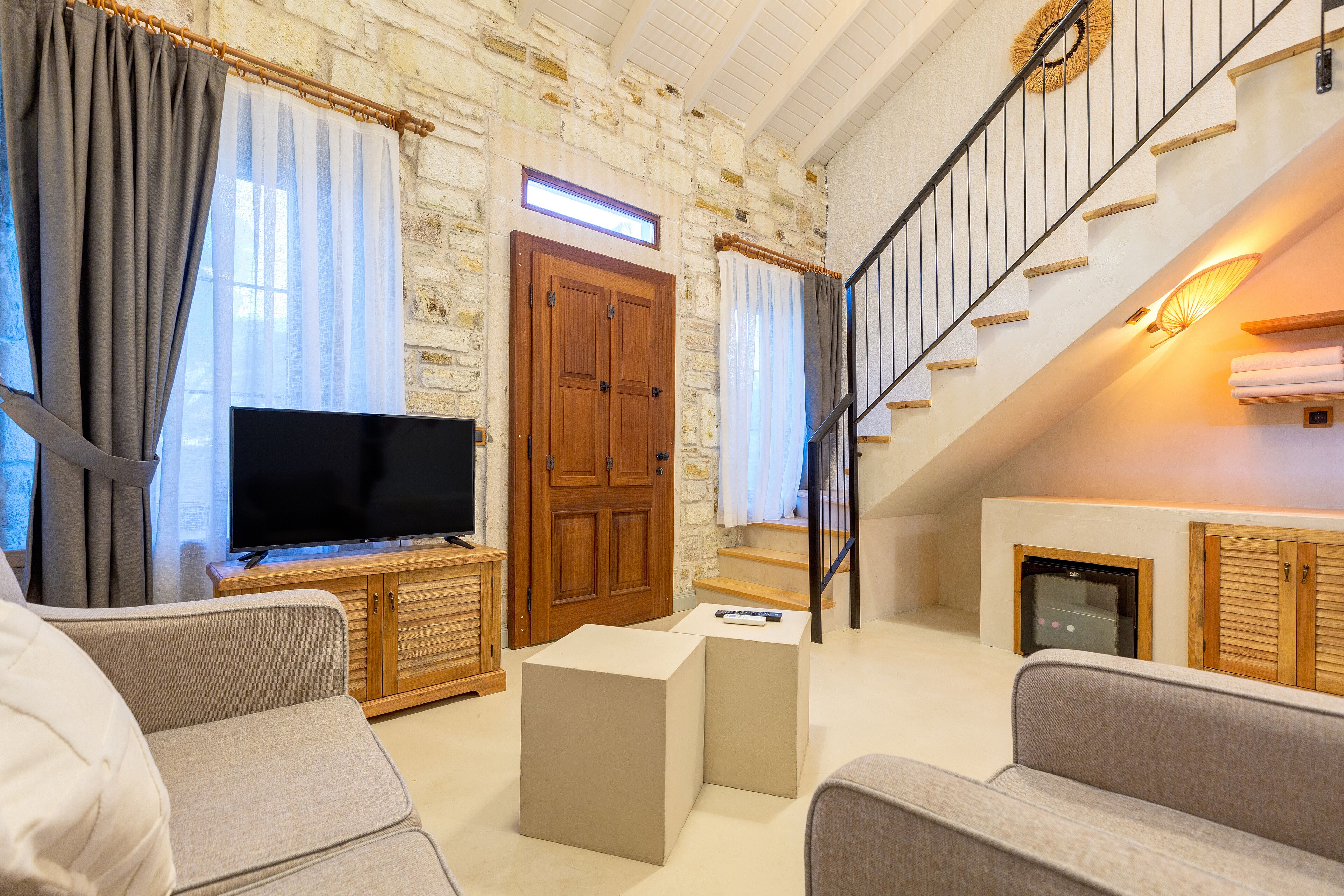 Ein Wohnzimmer mit Fernseher, Sofas, einer Holzkommode und einer Treppe.