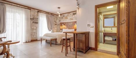 A cozy room with a bed, a wooden table, a bar area, and a bathroom visible through an open door.