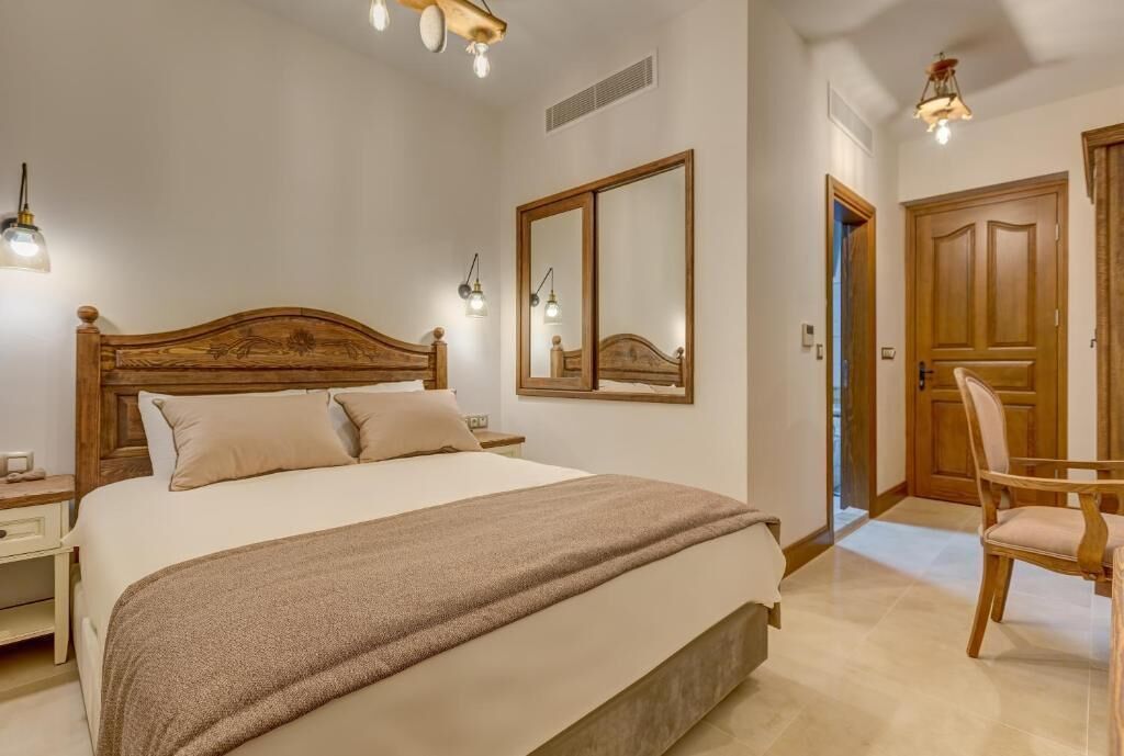A bedroom with a large bed, bedside lamps, a mirror, a wooden wardrobe, and a chair.