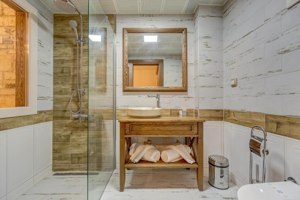 A bathroom with a glass shower enclosure, a wooden vanity with a sink, a mirror, and a towel rack.