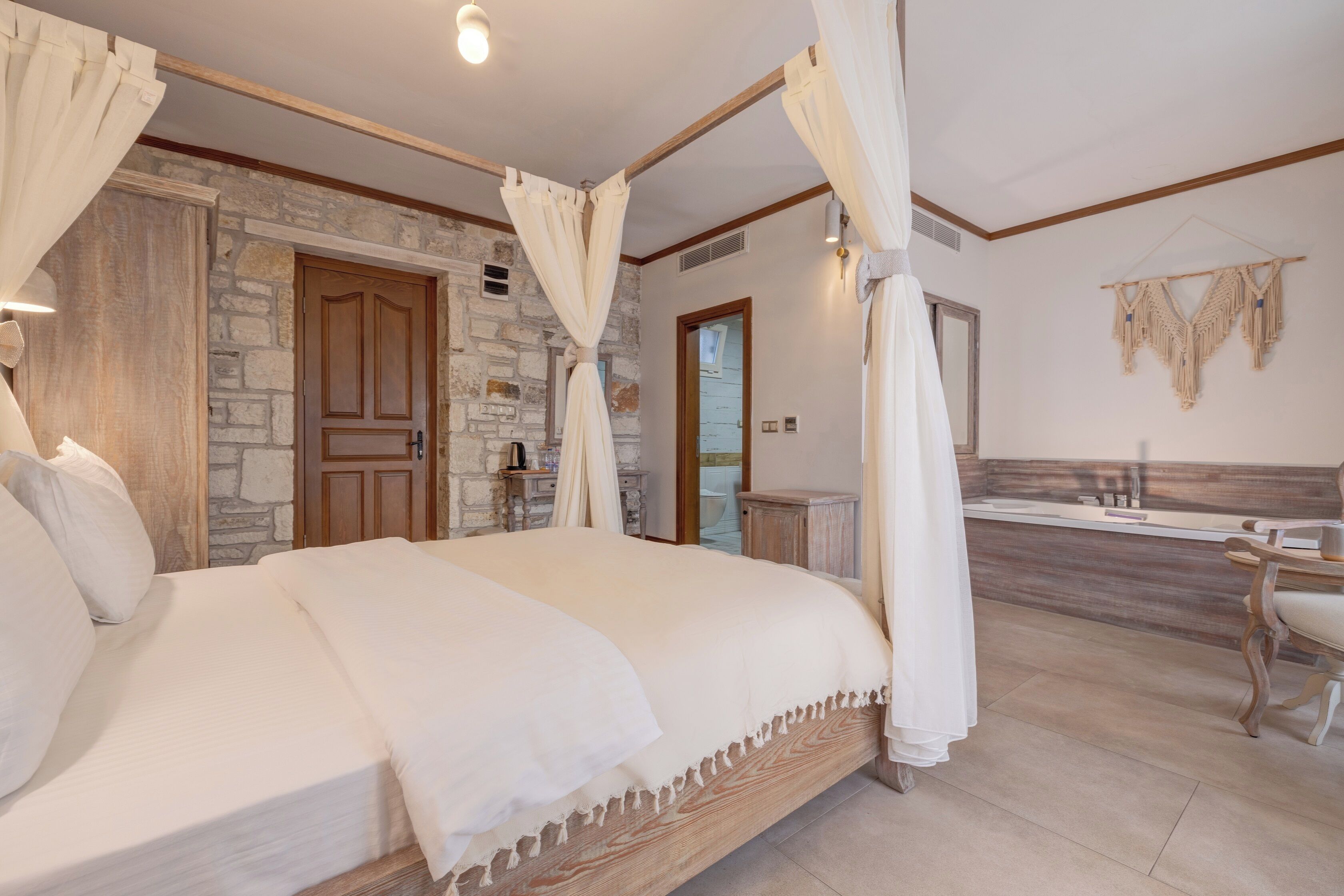 Een slaapkamer met een stenen muur, een houten deur, een bed met wit beddengoed en een kaptafel met spiegel.