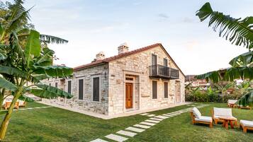 A stone house with a balcony, surrounded by a well-maintained lawn and tropical plants.