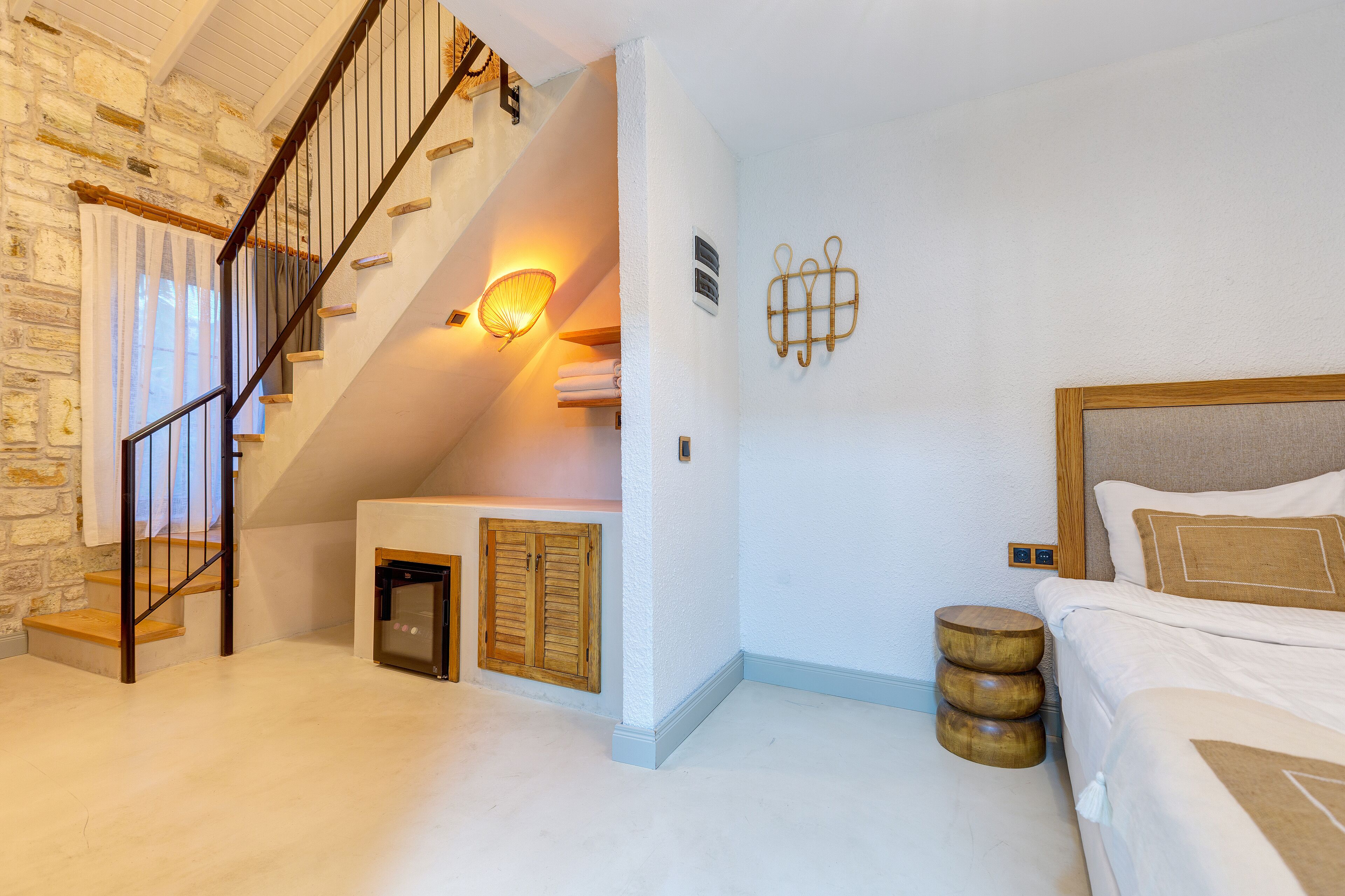 A bedroom with a wooden staircase, a bed with a headboard, and a wall-mounted light fixture.