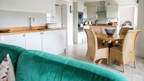 Eine moderne Küche mit weißen Schränken, einer Holz Arbeitsplatte und einem Essbereich mit Korbstühlen und einem Tisch.