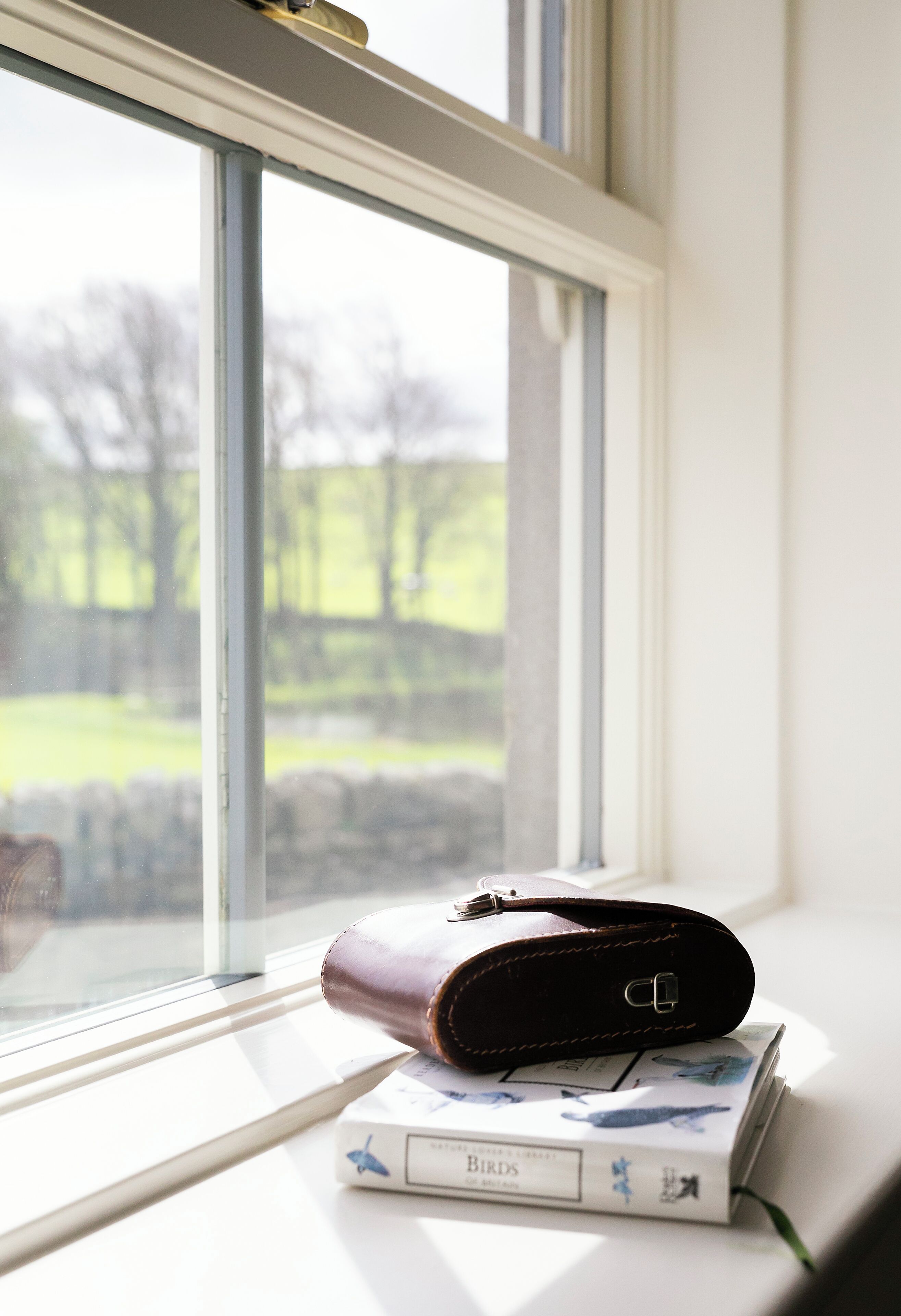 A window sill with a book and a brown leather case.