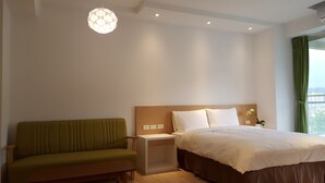 Une chambre d’hôtel avec un lit, un canapé vert, une table de chevet et un luminaire suspendu.