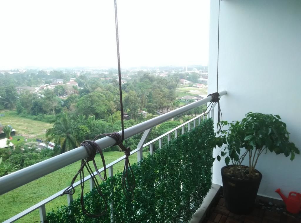 A balcony with a view of a green landscape, a potted plant, and a red watering can.
