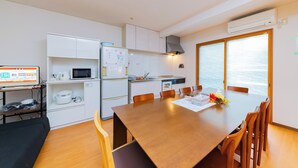 Une cuisine moderne avec des meubles blancs, un four à micro-ondes et une cuisinière. On y trouve une table à manger avec des chaises, et de grandes fenêtres offrent une vue sur la mer.