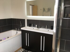 A modern bathroom with a bathtub, a sink, and a mirror. - Holway House (Sheringham)