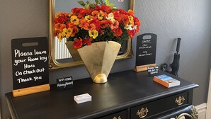 A hotel reception desk with a black console, gold accents, a large mirror, a vase of flowers, a sign instructing to leave room keys on checkout, and a WiFi sign. - Holway House (Sheringham)