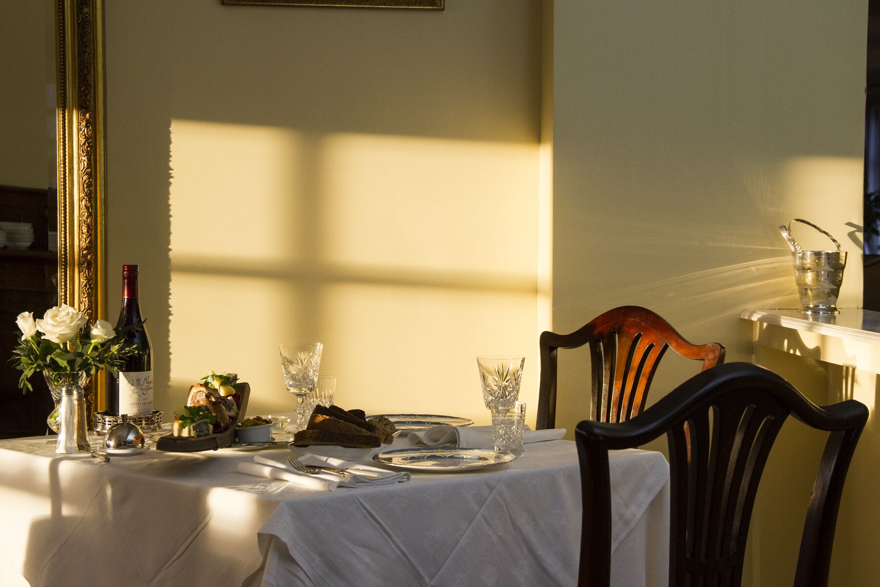 A dining table set with plates, glasses, and a bottle, with a chair and a mirror in the background.