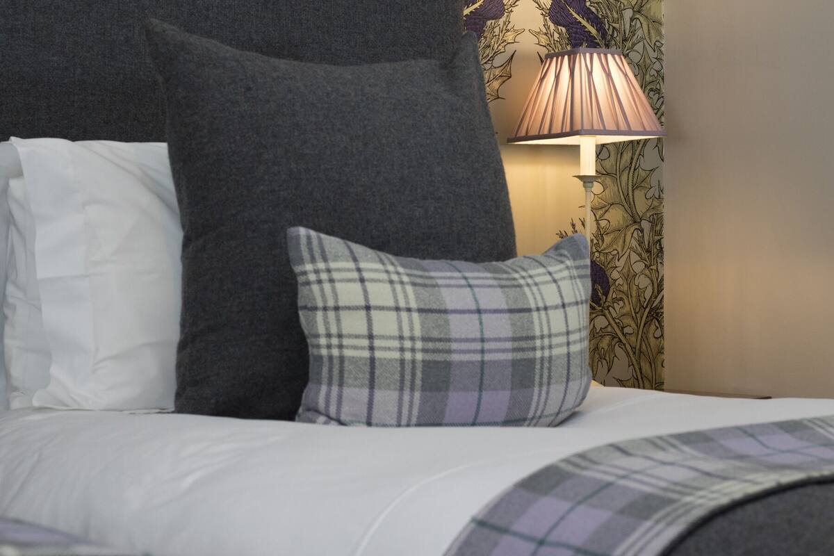 A bed with white bedding, a grey pillow, and a plaid pillow.
