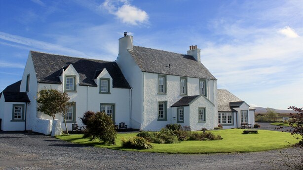 A large white house with a grey roof, multiple chimneys, and a well-maintained lawn. - Glenegedale House (Islay Island)