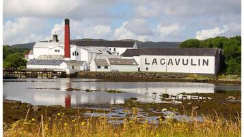 A historic building with a prominent chimney, named Lacavulin, situated by a body of water with a dock.