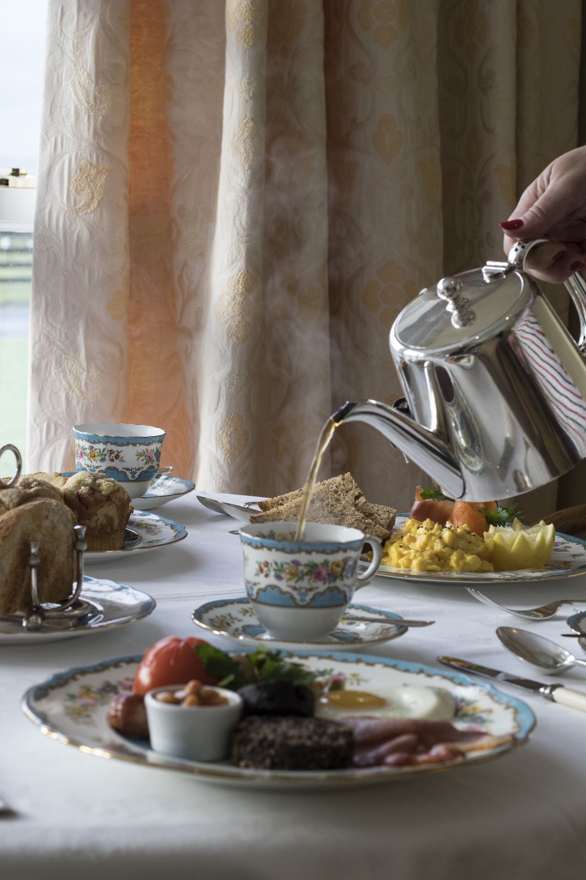 A breakfast setting with a variety of foods and a kettle pouring tea.