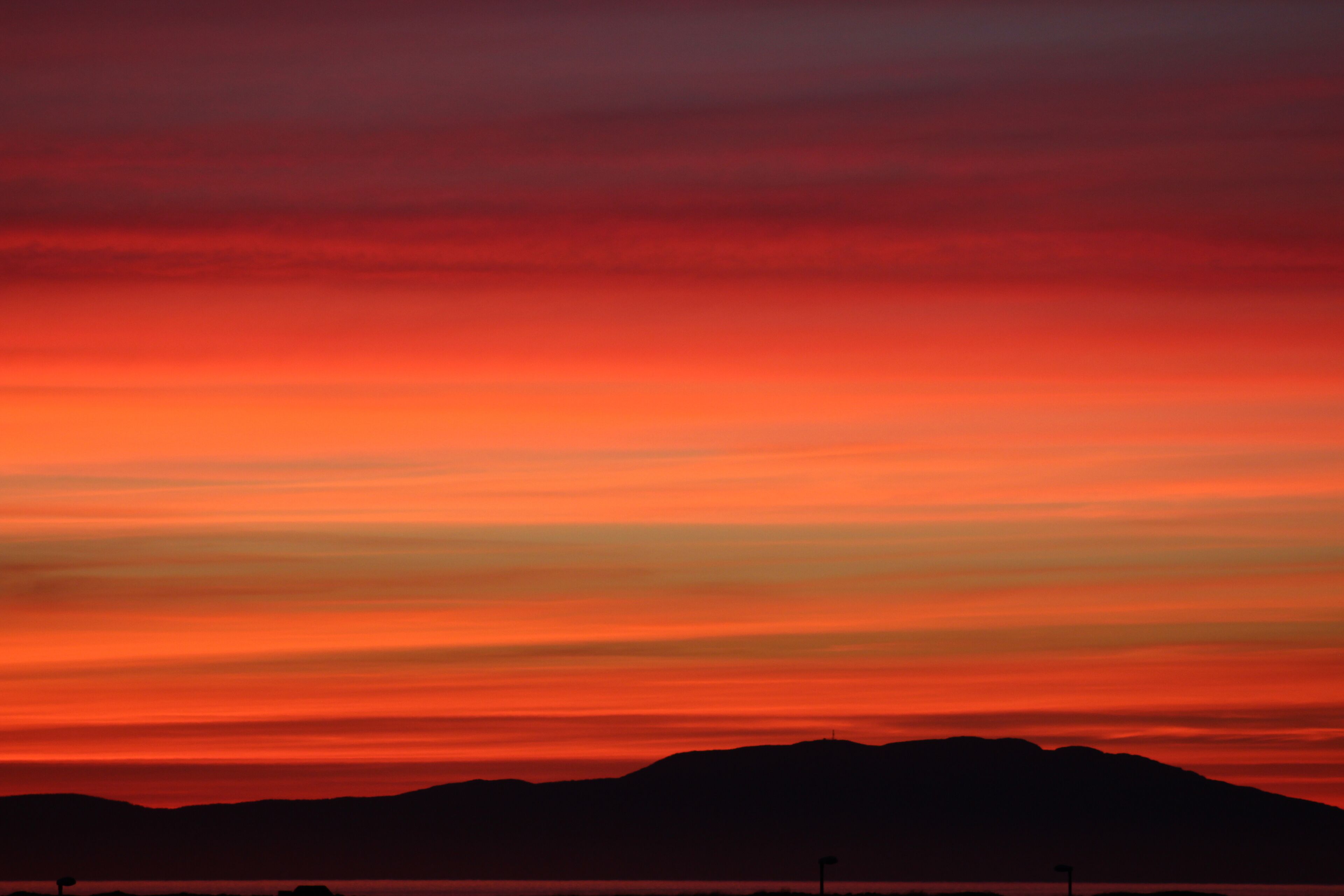 Solnedgang over et bjerglandskab med klar himmel.
