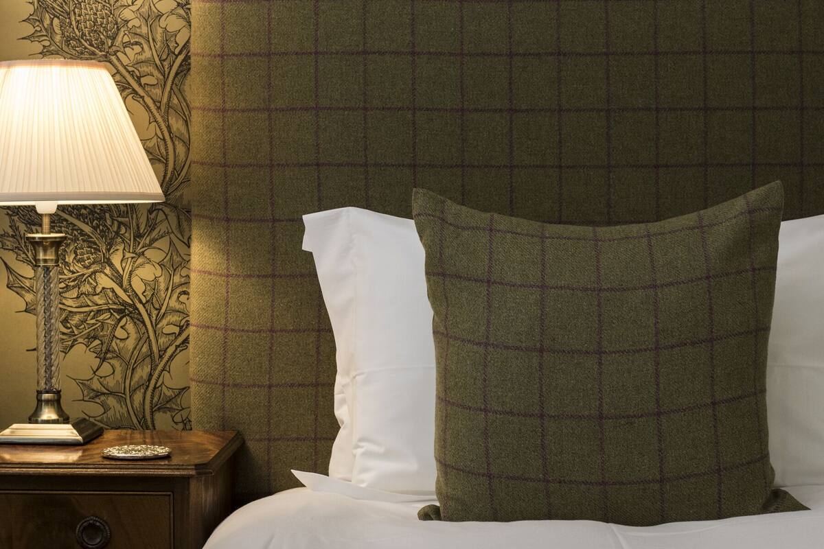 A hotel room with a bed, a nightstand with a lamp, and a wall with a floral pattern.