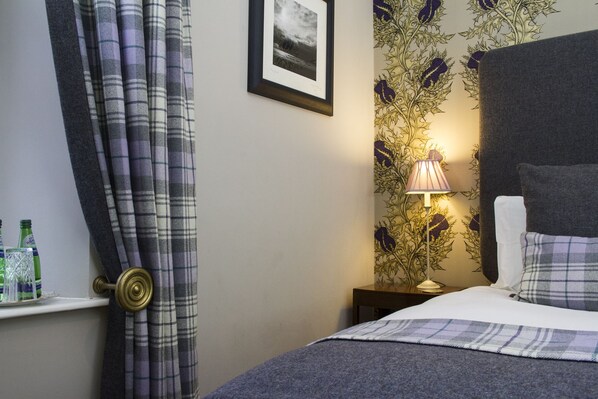 Habitación de hotel con cama, mesita de noche, lámpara y ventana con cortinas.