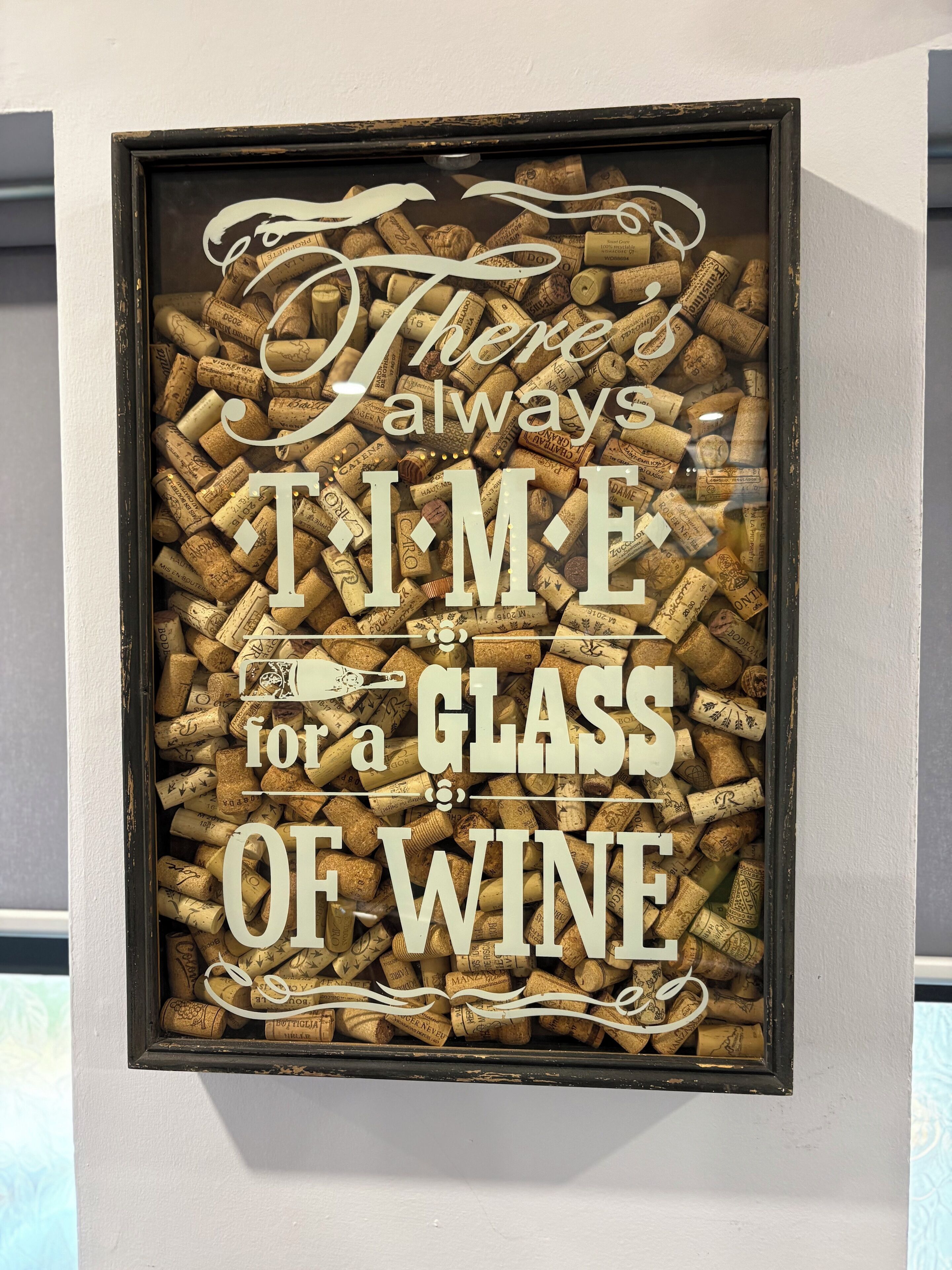 A framed sign with corks and text stating "There's always time for a glass of wine."