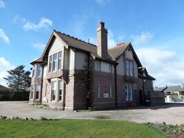 A two-story stone building with a chimney, large windows, and a sign indicating it is a hotel with a lounge and entrance.