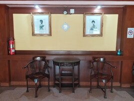 Un área de recepción con dos retratos enmarcados en la pared, una pequeña mesa y dos sillas ornamentadas.
