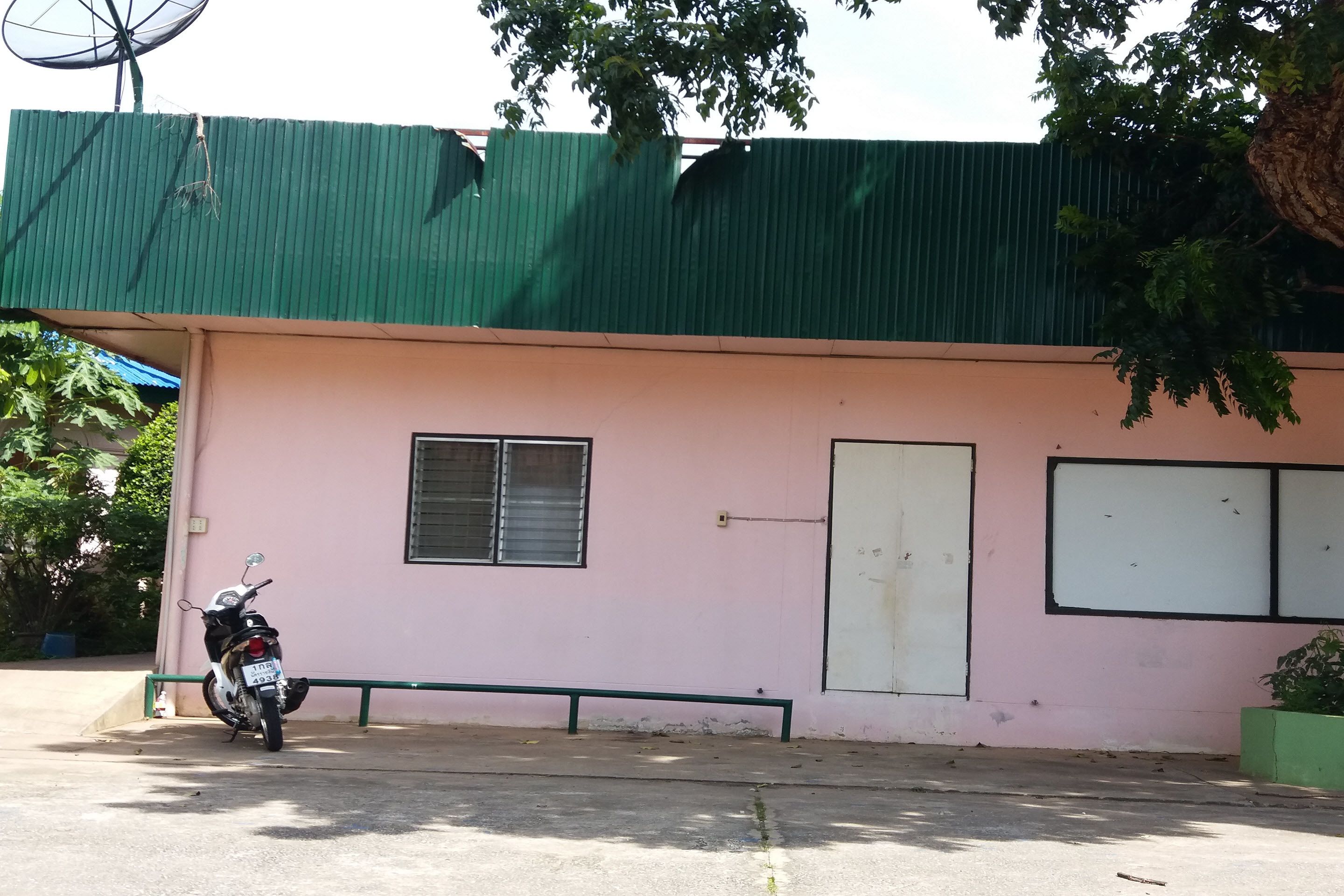 Un edificio rosa con techo verde, una motocicleta estacionada adelante y una antena parabólica en el techo.