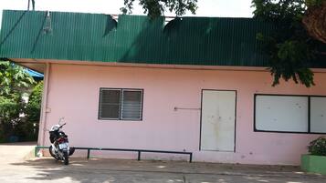 Un edificio rosa con techo verde, una motocicleta estacionada adelante y una antena parabólica en el techo.