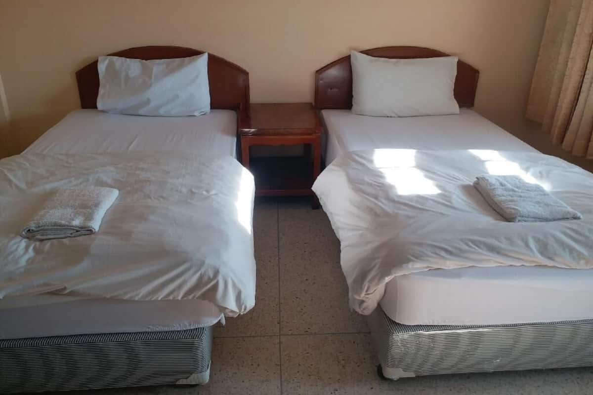 Hotellihuone, jossa on kaksi erillistä sänkyä, yöpöytä ja ikkuna, jossa on verhot.