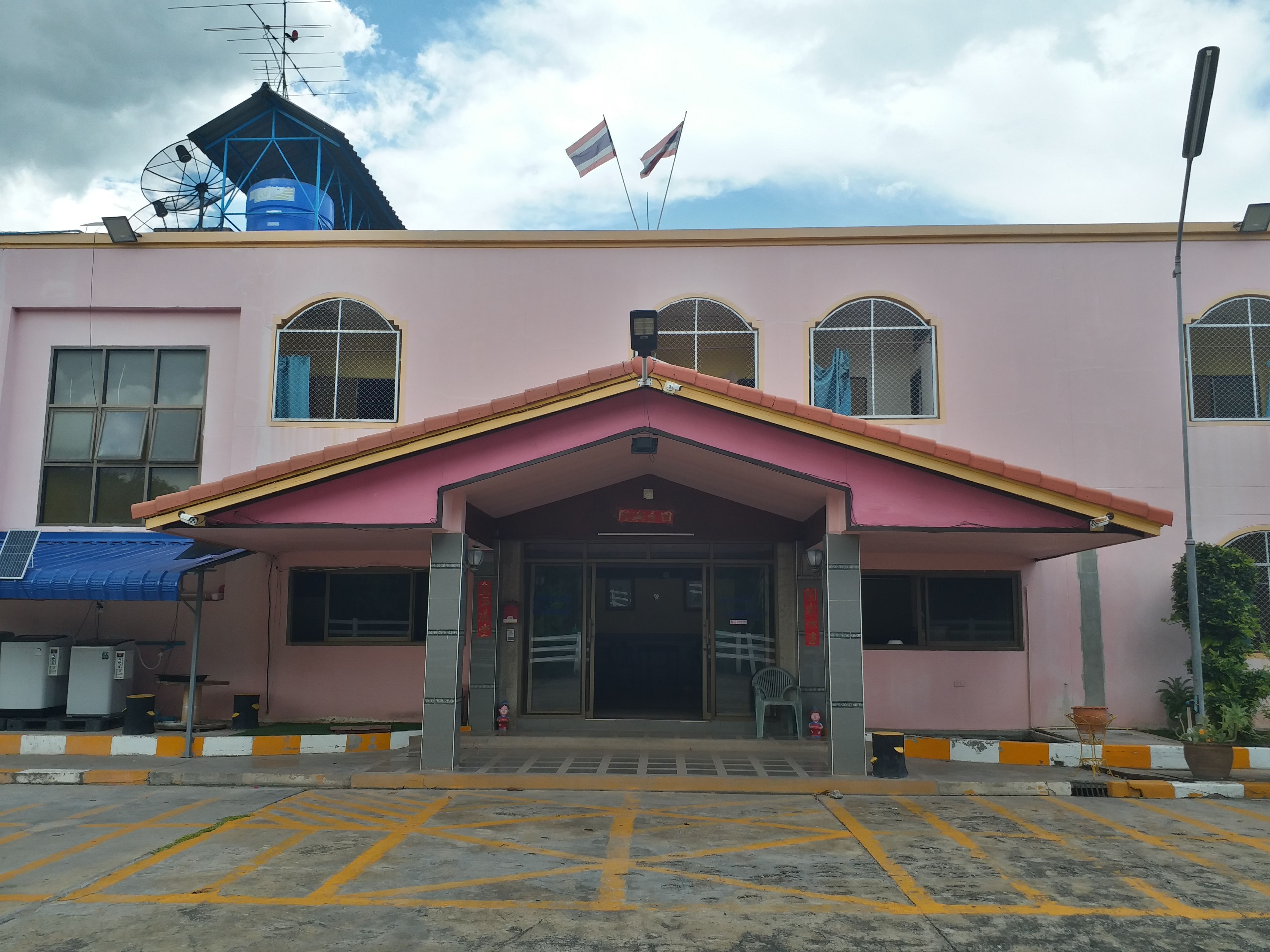 A building with a pink facade, a central entrance with a red roof, and a blue water tank on the roof.