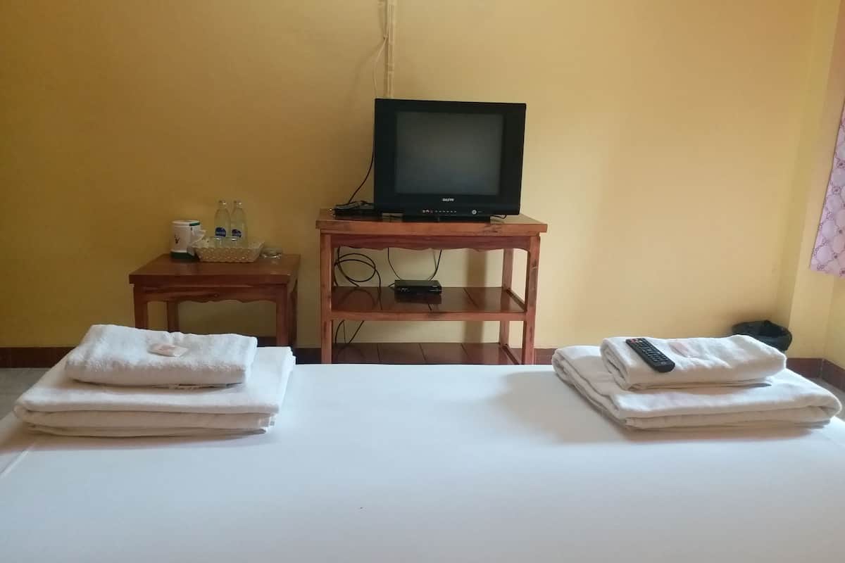 Hotellihuone, jossa on sänky, puinen jalusta, jonka päällä on televisio, pieni pöytä, jossa on hygieniatarvikkeita, ja kaukosäädin sängyllä.