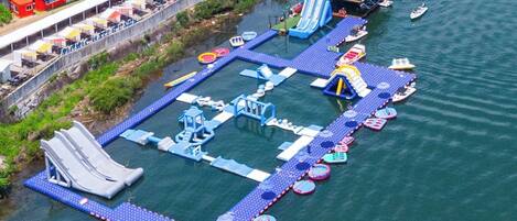 An aerial view of a water park with multiple slides, inflatable rafts, and a dock with boats.