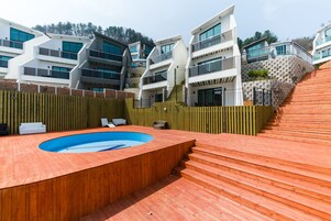 Un edificio moderno con zona de piscina, terraza de madera y escaleras que llevan a un balcón.