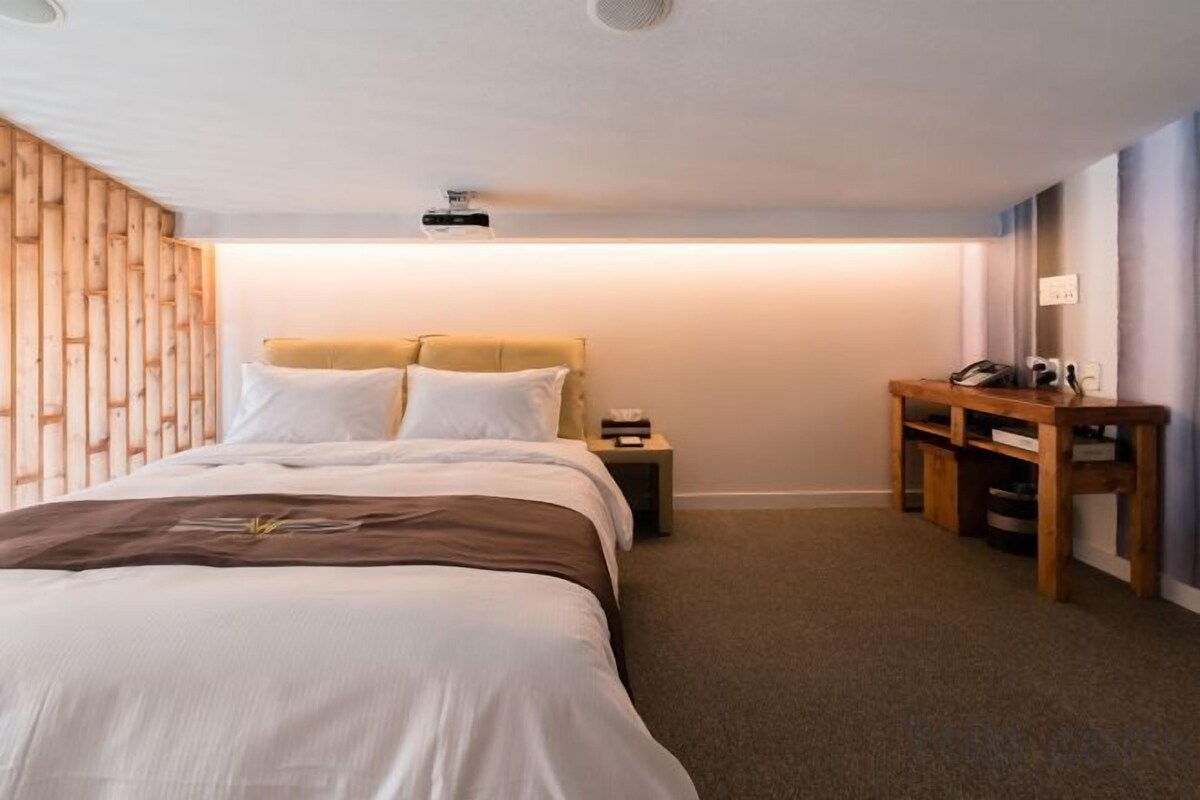 Un dormitorio con cama, mesitas de noche, escritorio y proyector de pared.