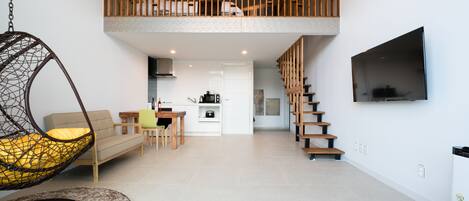 Un espacio de estar moderno con una silla colgante, sofá, comedor, cocina y una escalera que lleva a un altillo.
