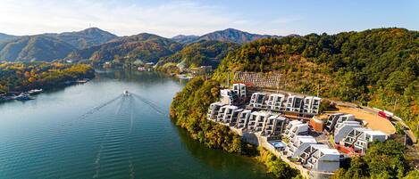 Un hotel a orillas del río con varias construcciones, un muelle para embarcaciones y colinas boscosas circundantes.