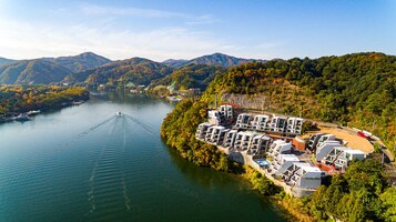 A riverside hotel with multiple buildings, a boat dock, and surrounding forested hills.
