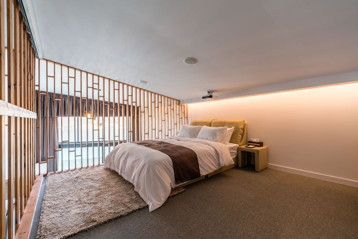 Ein modernes Schlafzimmer mit Bett, Nachttisch, kleinem Tisch und Blick durch eine Holzwand.