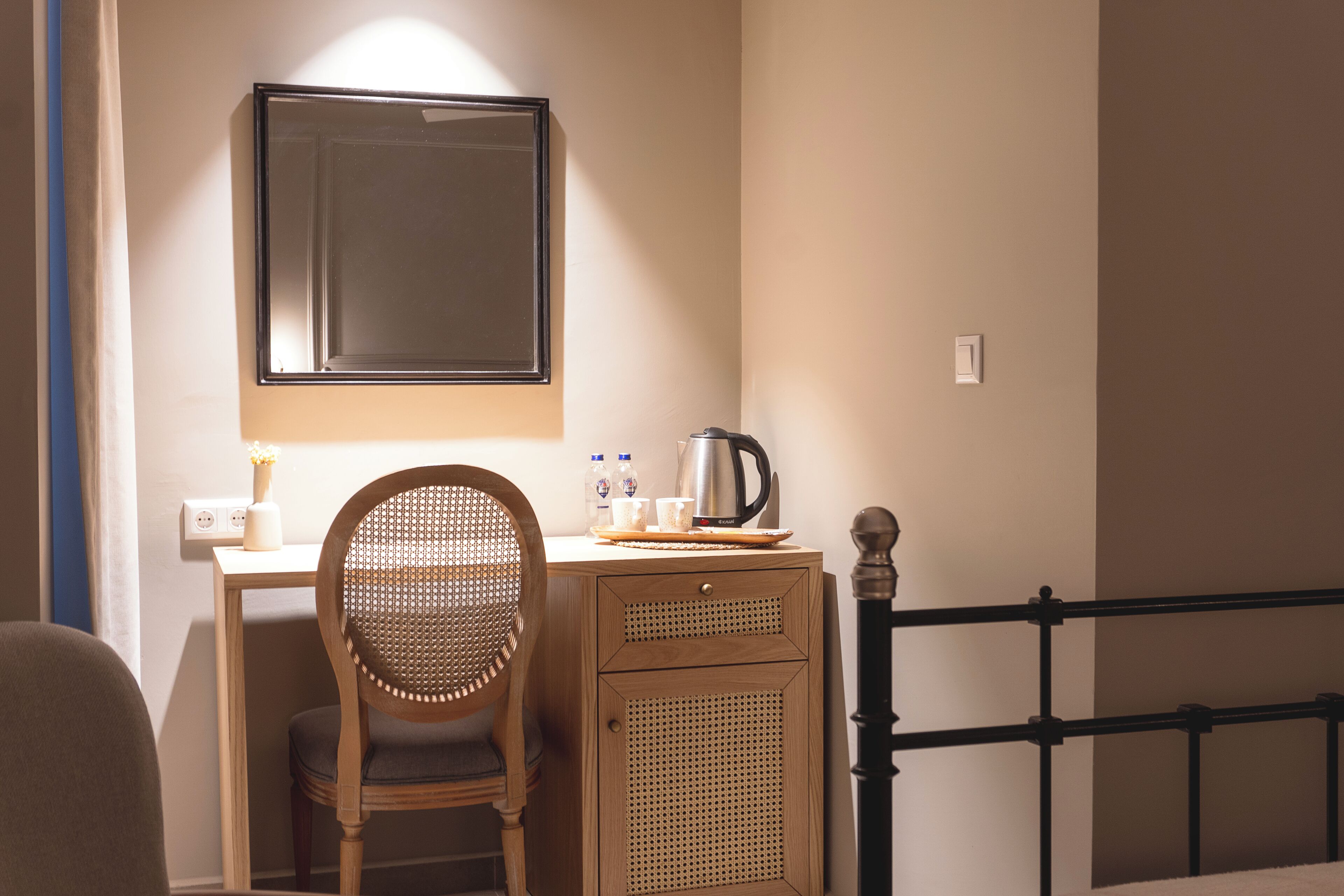 Ein Hotelzimmer mit einem Holztisch, einem Stuhl, einem Bett mit schwarzem Metallgestell, einem Spiegel an der Wand und einem kleinen Schrank.