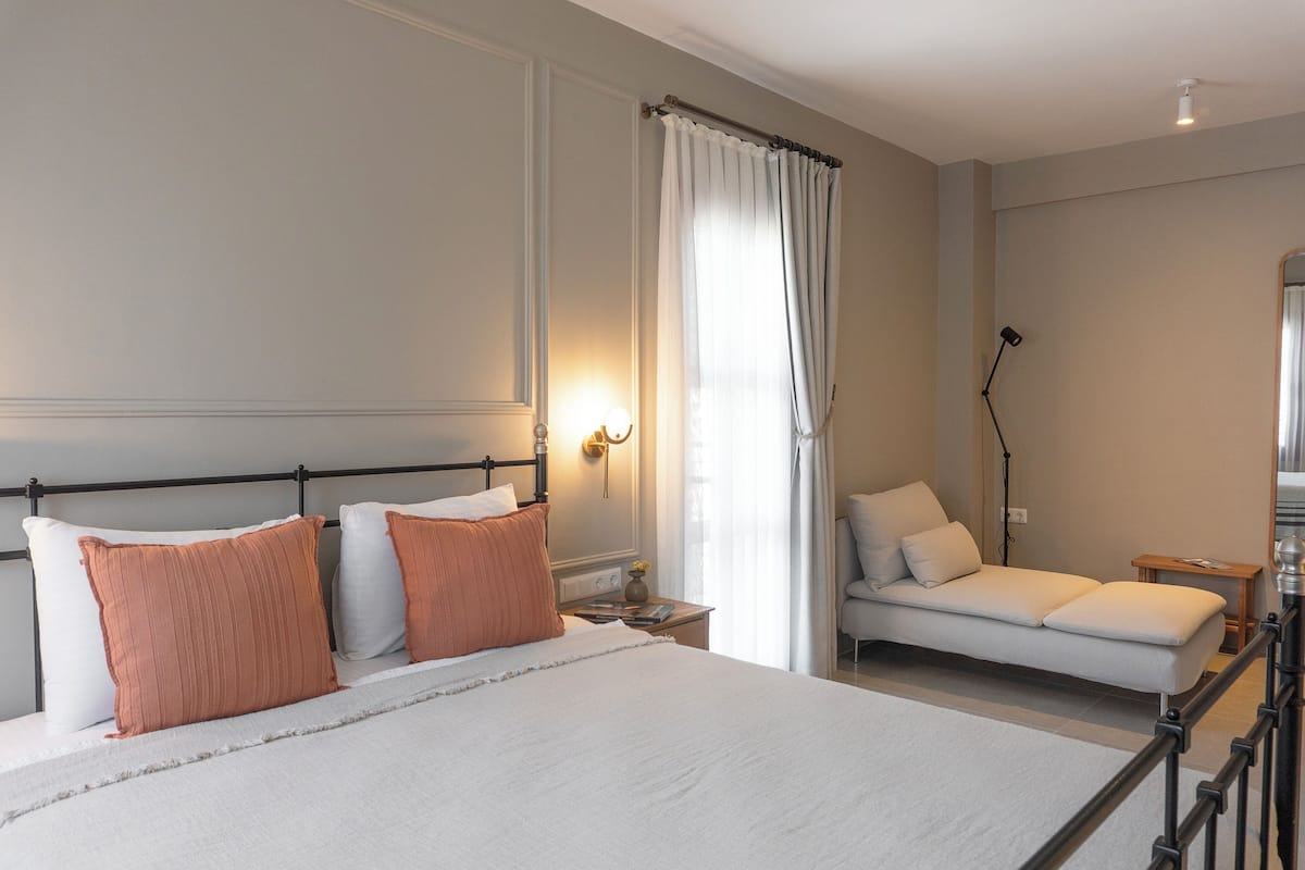 A bedroom with a large bed, a sofa, a nightstand, and a lamp.