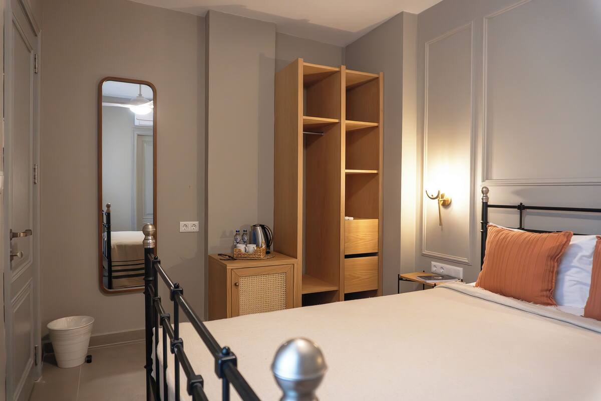 A bedroom with a bed, a wardrobe, a bedside table, a mirror, and a wall-mounted light fixture.