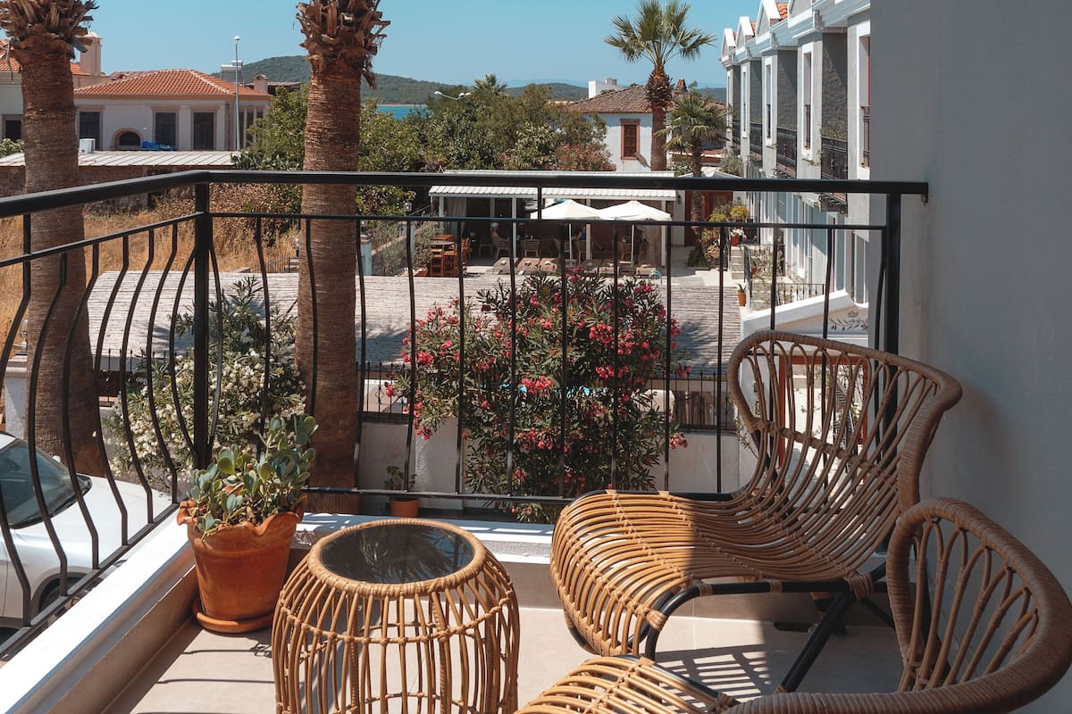 A balcony with wicker furniture, a potted plant, and a view of a coastal town.