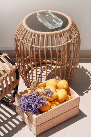 A wicker chair with a glass top and a wooden crate filled with lemons and purple flowers. - Kapya Cunda (Ayvalik)