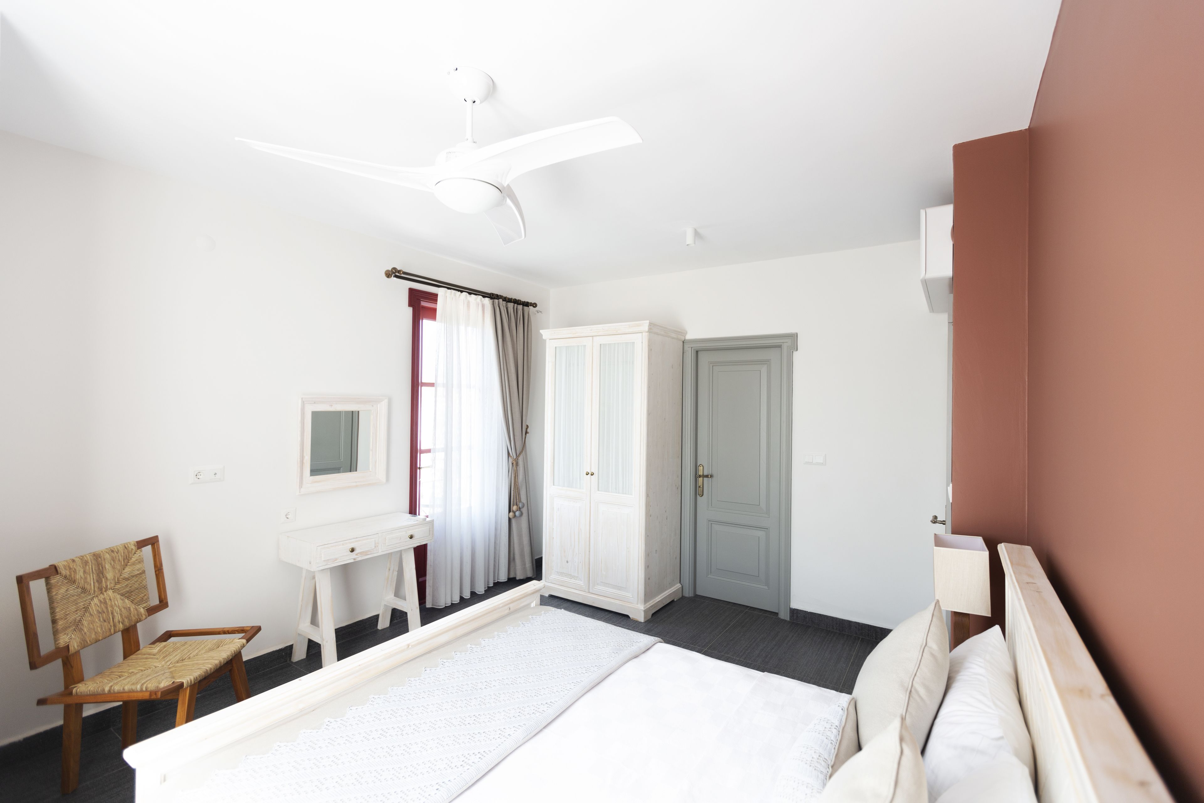 A bedroom with a bed, a desk, a chair, a wardrobe, and a ceiling fan.