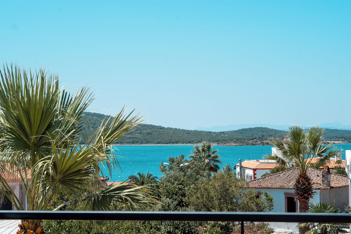 A coastal view with a clear sky, a turquoise sea, and a mountainous backdrop.