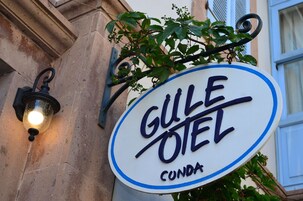 Placa para "GULE OTEL" com luminária e vegetação.