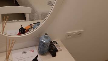 A hotel room with a bed, a bedside table with a mirror, a small table with a vase, a remote control, and a piece of paper.