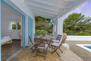 A covered outdoor dining area with a table set for four, surrounded by wooden chairs.