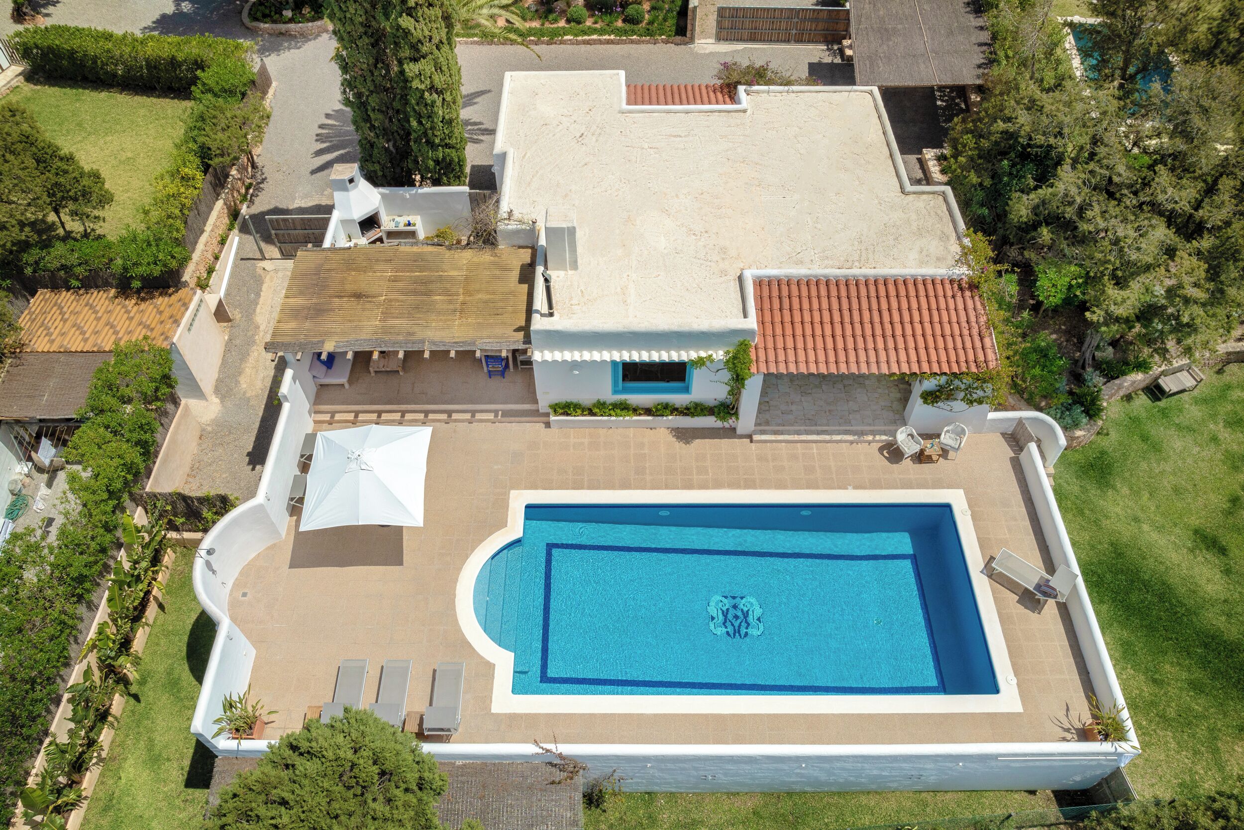 An aerial view of a house with a large rectangular swimming pool, a covered patio area, and a well-maintained lawn.