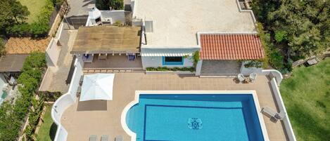 An aerial view of a house with a large rectangular swimming pool, a covered patio area, and a well-maintained lawn.