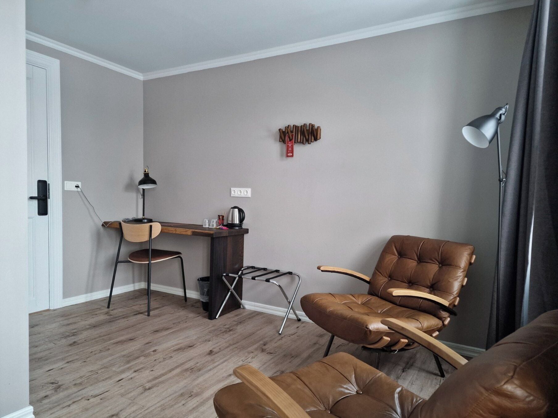 Un salon moderne avec un plancher en bois, un bureau avec une chaise, un fauteuil en cuir marron et une lampe sur pied.